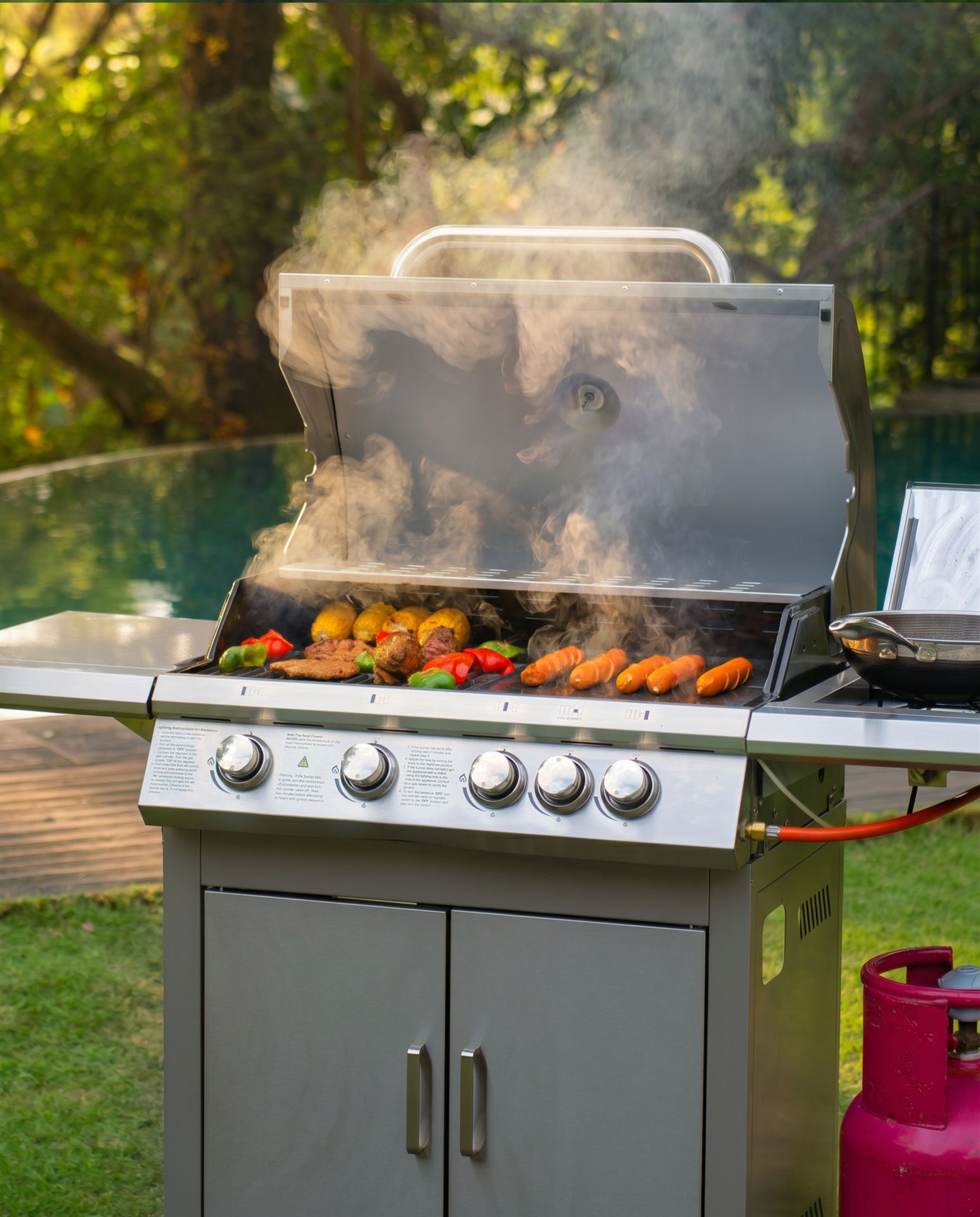 Grill in use with smoke rising, food on the grates, villa pool behind